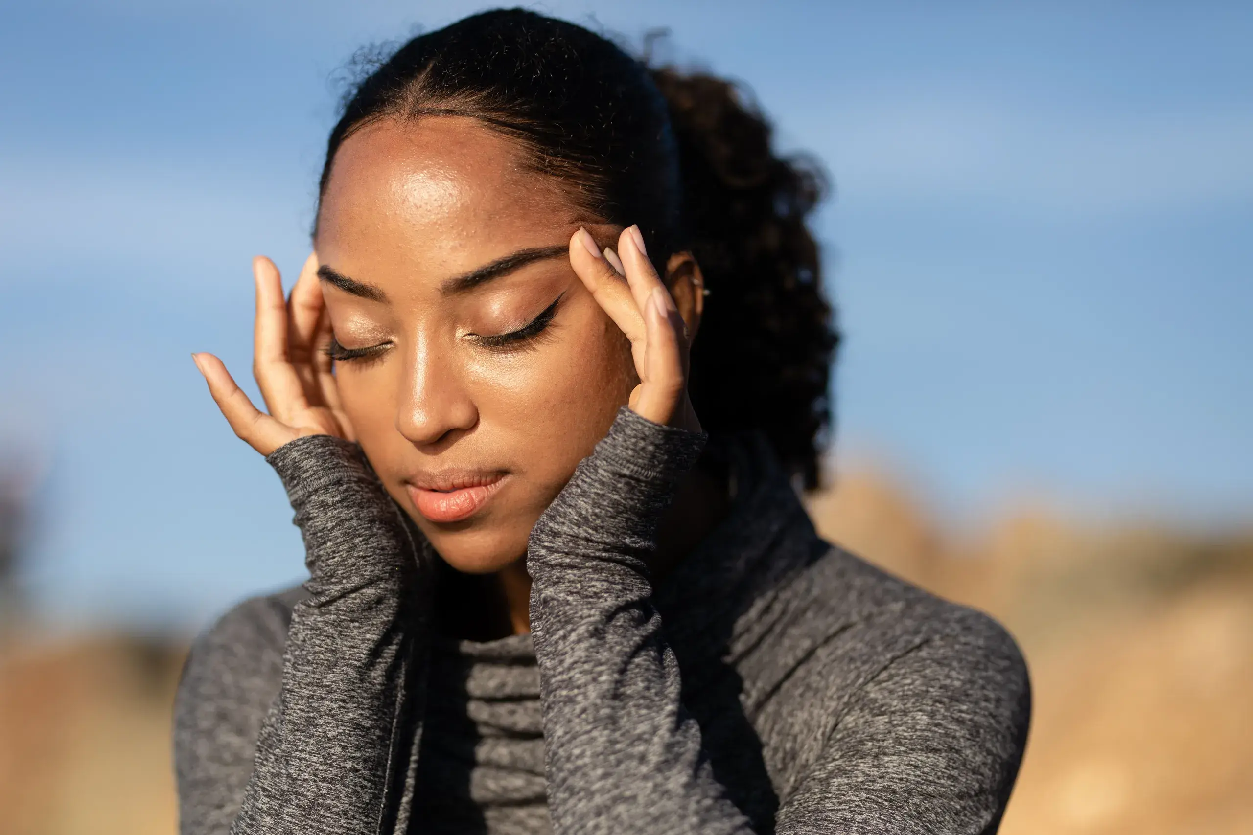 A woman pressing her temples with her eyes closed, in discomfort.