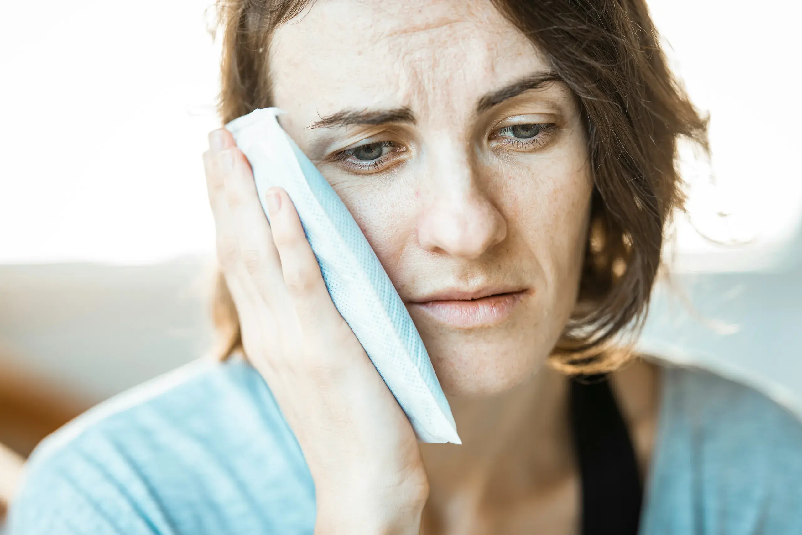 A woman holding a cold pack against her jaw.