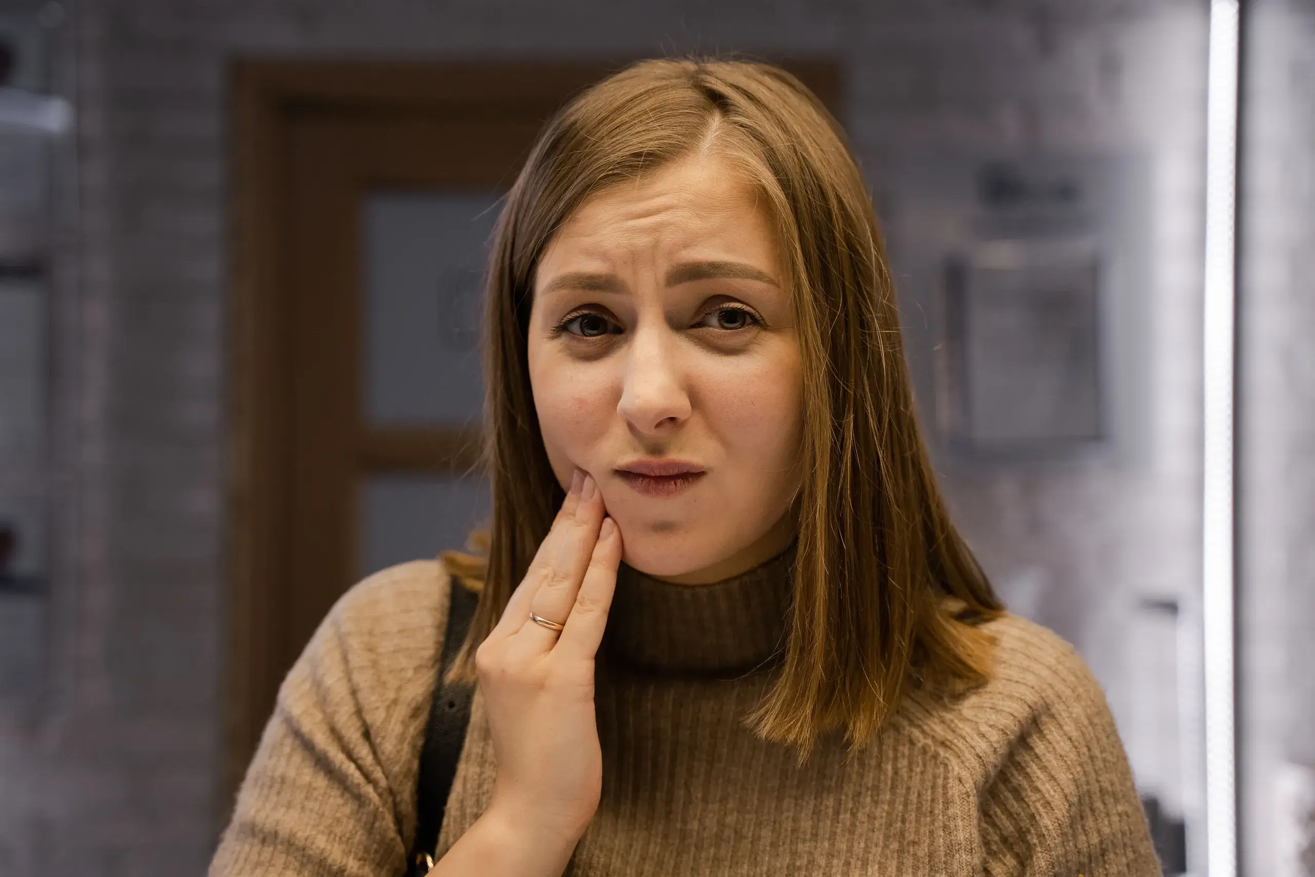A woman holding her cheek with a pained expression from facial pain.