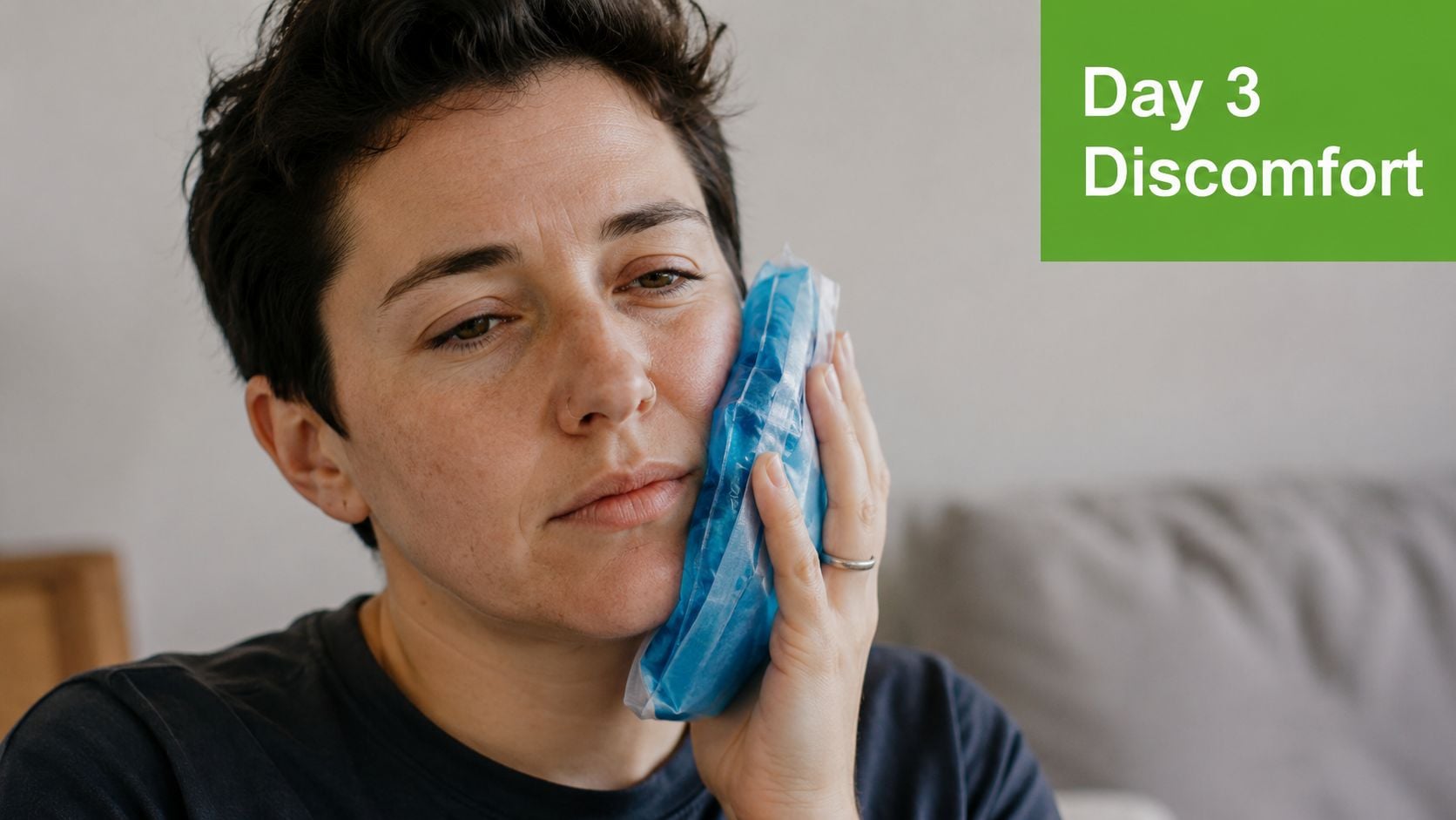 A person with short hair holding a cold blue ice pack against their swollen jaw after surgery.