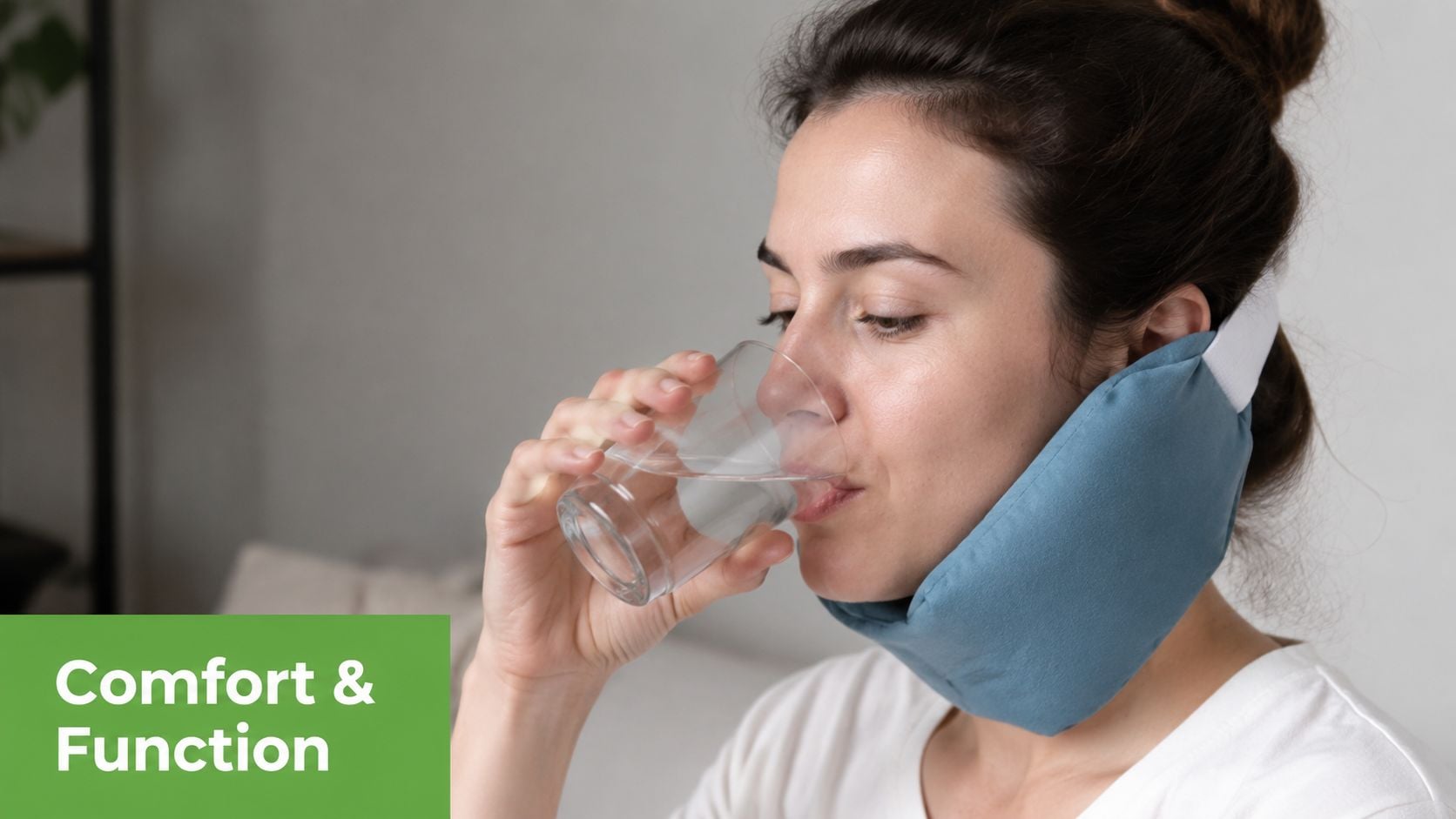 A woman wearing a blue ice pack wrap around her jaw while drinking a glass of water.