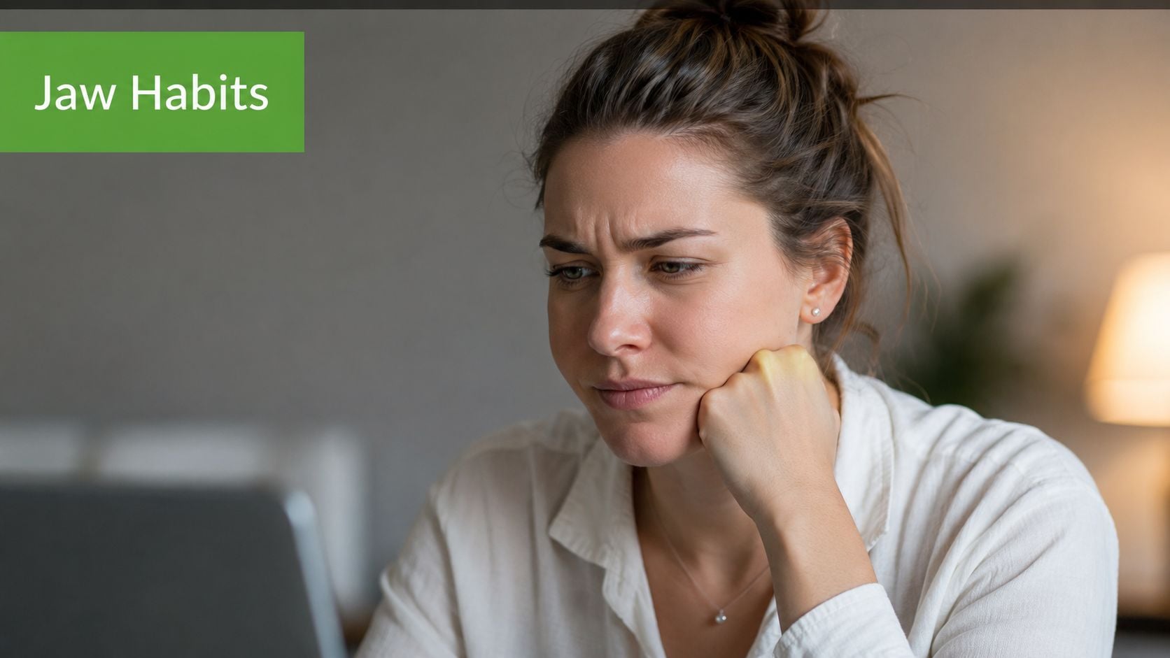 A woman looks concerned while resting her chin on her hand while working on a laptop.